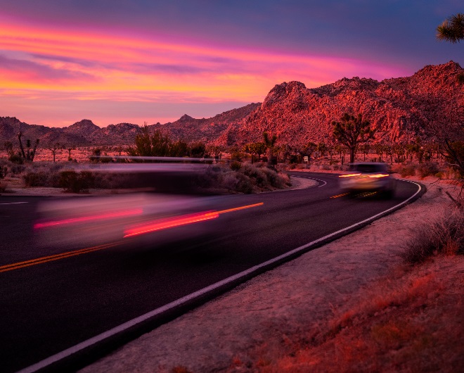 A winding road with a car traveling quickly during sunset